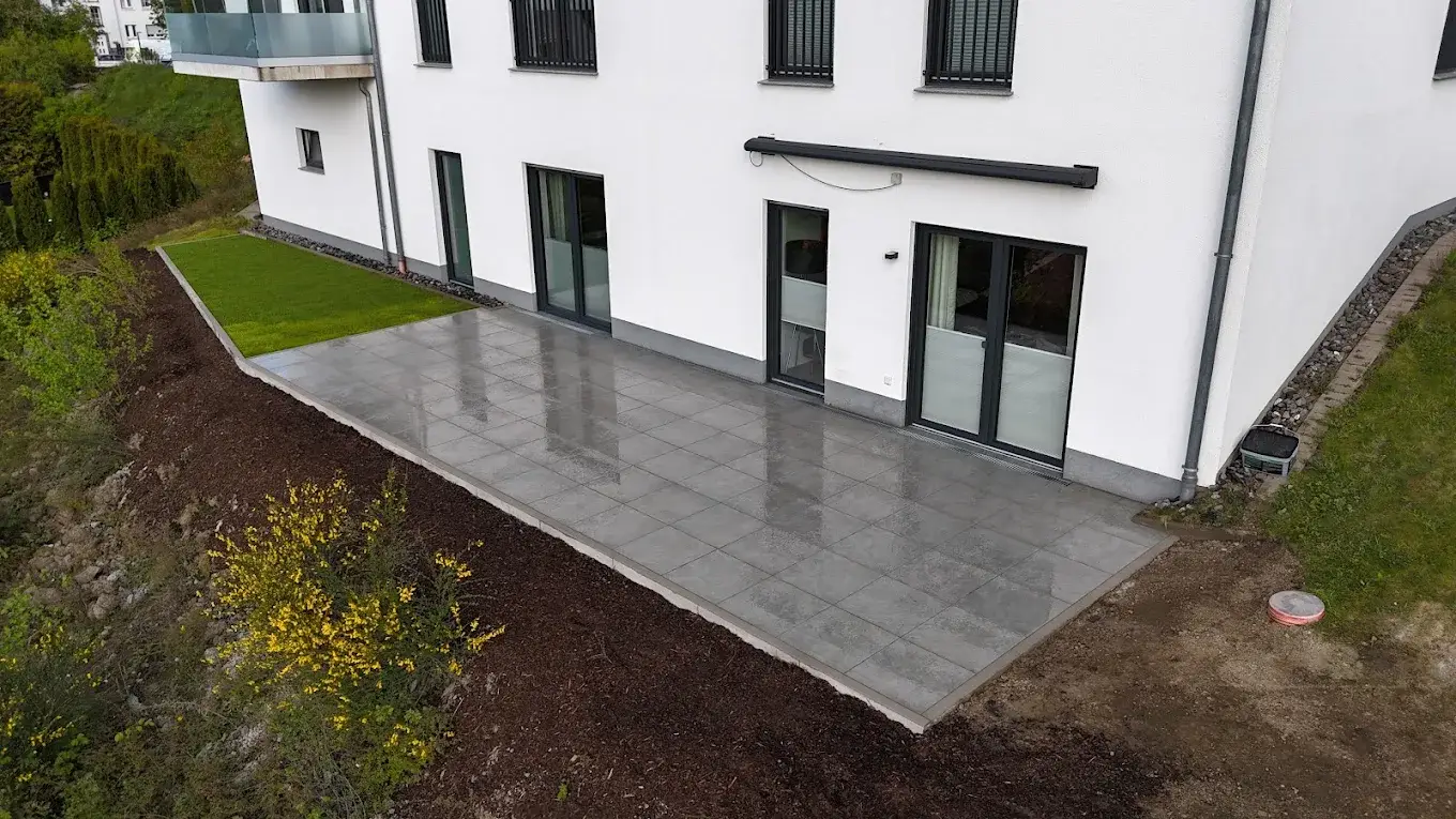 Neue Terrasse mit grauen Platten an der Hauswand