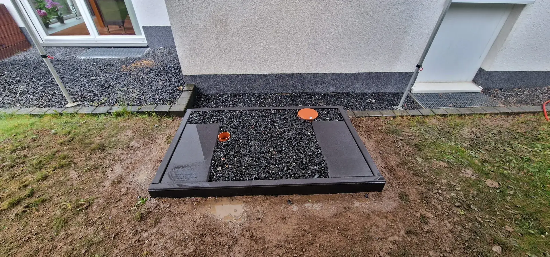 Fertiges Wärmepumpen-Fundament mit Kiesbett an der Hauswand
